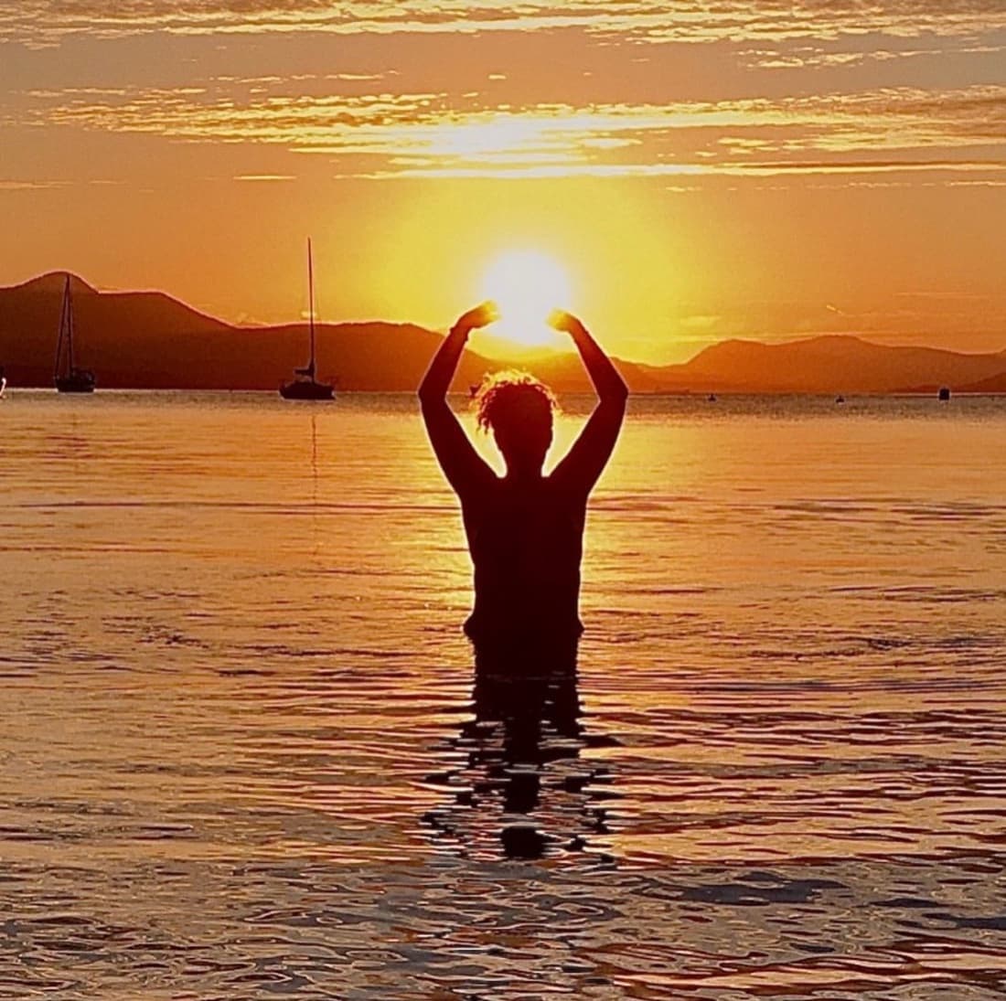 Sunrise over the water, arms cradling the sun — the Rise & Shine retreat
